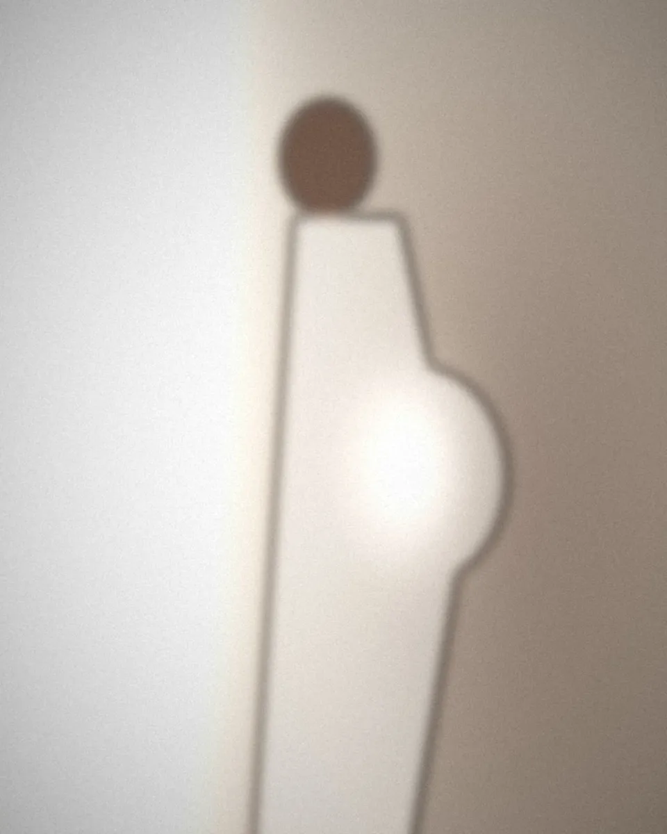 Future maman de profil près d’une fenêtre, vêtue d’une robe claire
